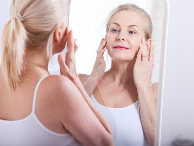 Middle aged woman looking at wrinkles in mirror
