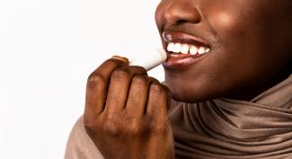 Black woman applying lip balm against a white background