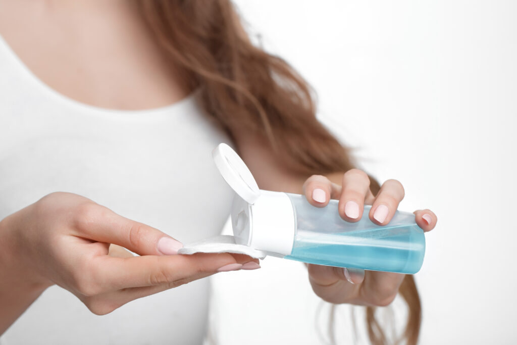 Woman's hands pouring toner onto cotton pad.