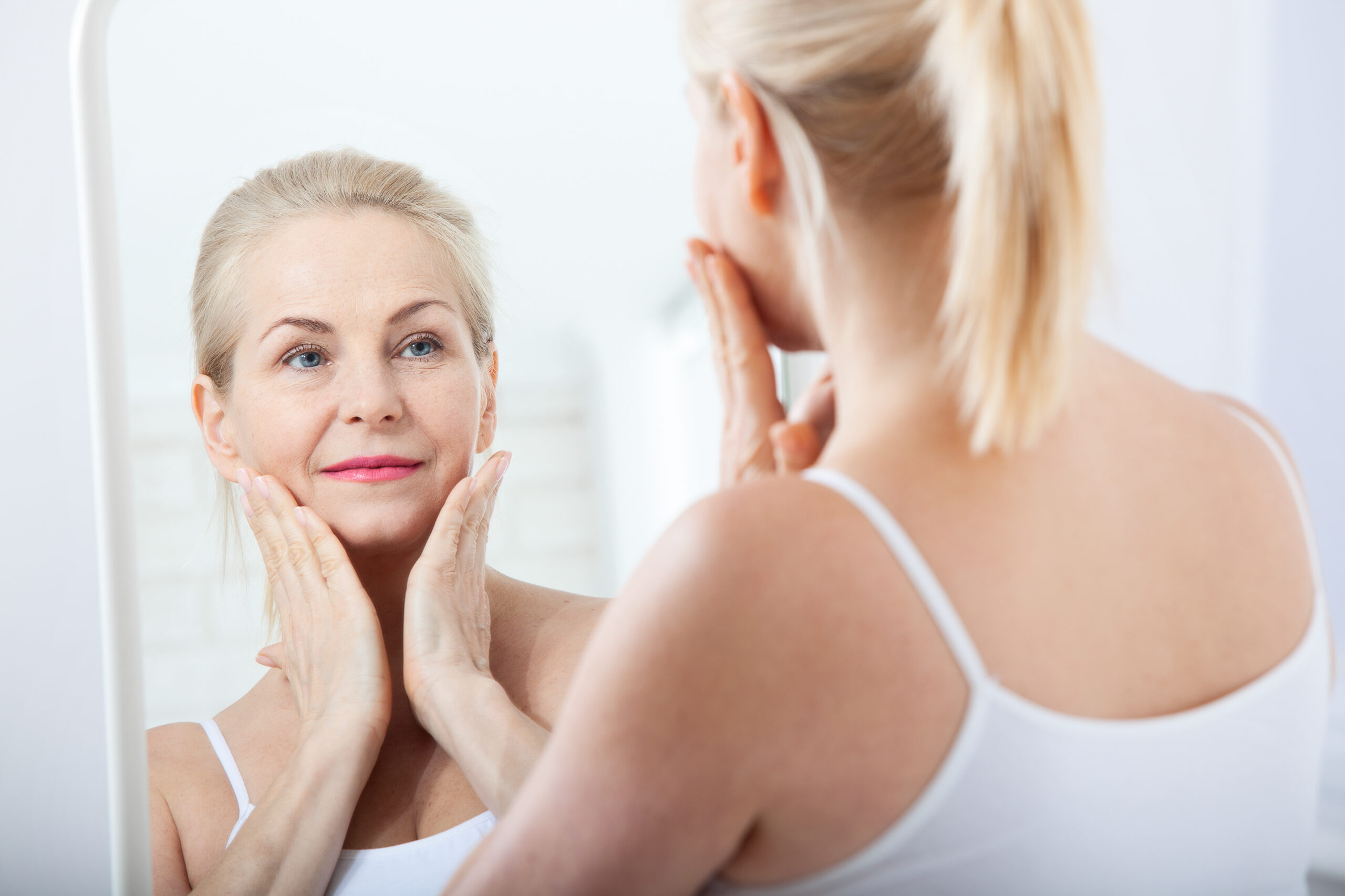 Woman looking at wrinkles in a mirror.